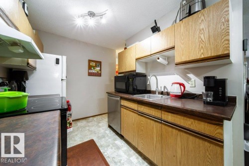 Functional kitchen featuring wood-finish cabinetry, dark countertops, and a stainless steel sink - #307 6212 180 St Nw, Edmonton, AB - Indoor Photo Showing Kitchen