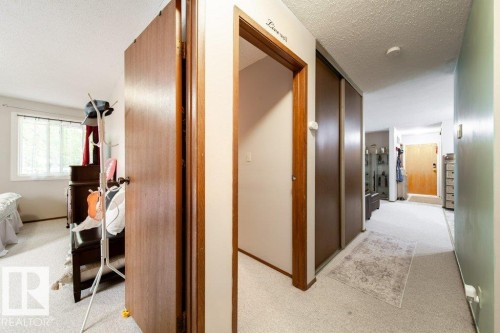 Carpeted hallway with wood-finish doors and trim, featuring a light-colored wall and a contrasting green wall - #307 6212 180 St Nw, Edmonton, AB - Indoor Photo Showing Other Room
