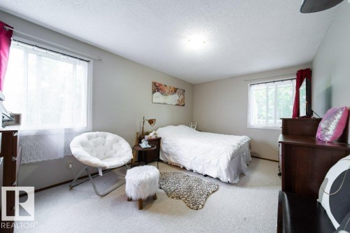 Carpeted bedroom featuring two windows with white sheer curtains, neutral wall paint, and a textured ceiling - #307 6212 180 St Nw, Edmonton, AB - Indoor Photo Showing Bedroom