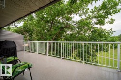 Expansive covered balcony featuring a textured gray surface, white metal railing, and mature green trees - 