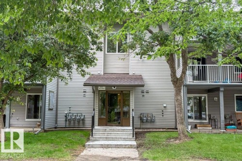 Multi-level building exterior featuring light gray horizontal siding and a central entryway with a small overhang - #307 6212 180 St Nw, Edmonton, AB - Outdoor