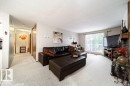 Spacious living area featuring light-colored carpeting, a large sliding glass door, and an exposed brick fireplace - #307 6212 180 St Nw, Edmonton, AB  - Indoor Photo Showing Living Room 