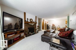 Spacious living area featuring a brick fireplace with a wood mantle, white textured ceilings, light-colored carpeting, and a recessed fireplace opening - 