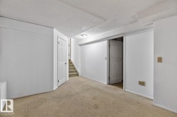 Finished lower level featuring neutral carpeting, white trim, and a white six-panel door - 