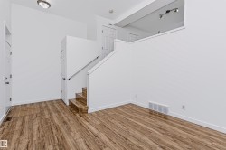 Open living space featuring wood-finish flooring, white walls, and a staircase with a white railing - 
