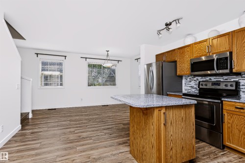 Kitchen featuring wood-finish cabinetry, stainless steel appliances, a mosaic tile backsplash, and a granite-look island with breakfast bar seating - #66 8304 11 Av Sw, Edmonton, AB - Indoor Photo Showing Kitchen With Stainless Steel Kitchen