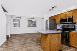 Kitchen featuring wood-finish cabinetry, stainless steel appliances, a mosaic tile backsplash, and a granite-look island with breakfast bar seating - 