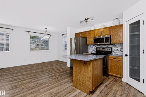 Open-concept kitchen and dining area featuring wood-finish flooring, a kitchen island with a speckled countertop, stainless steel appliances, and a tiled backsplash - #66 8304 11 Av Sw, Edmonton, AB - Indoor Photo Showing Kitchen