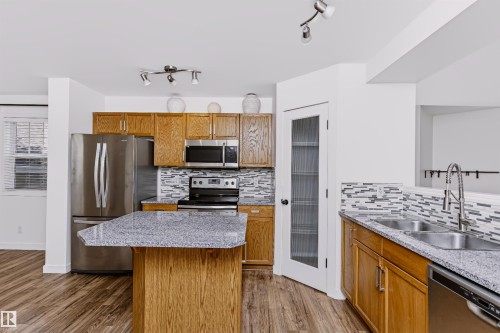Kitchen with wood-finish flooring, stainless steel appliances, and an island with a breakfast bar - #66 8304 11 Av Sw, Edmonton, AB - Indoor Photo Showing Kitchen With Stainless Steel Kitchen With Double Sink