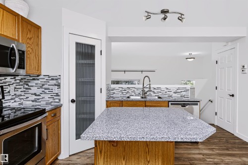 Kitchen featuring a multi-tone tile backsplash, stainless steel appliances, wood-finish flooring, and a central island with a granite-style countertop - #66 8304 11 Av Sw, Edmonton, AB - Indoor Photo Showing Kitchen With Double Sink With Upgraded Kitchen