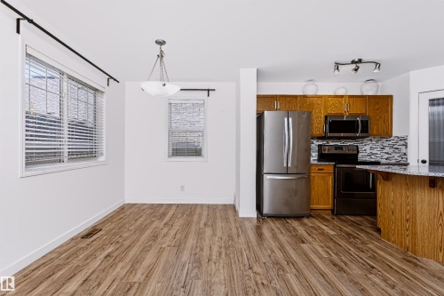 Open-concept living area featuring wood-finish flooring, white walls, and multiple windows with blinds - #66 8304 11 Av Sw, Edmonton, AB - Indoor Photo Showing Kitchen