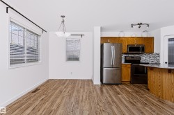 Open-concept living area featuring wood-finish flooring, white walls, and multiple windows with blinds - 