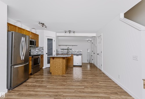 Open-concept kitchen featuring wood-finish flooring, a central island with a stone-finish countertop, stainless steel appliances, and a mosaic tile backsplash - #66 8304 11 Av Sw, Edmonton, AB - Indoor Photo Showing Kitchen With Stainless Steel Kitchen