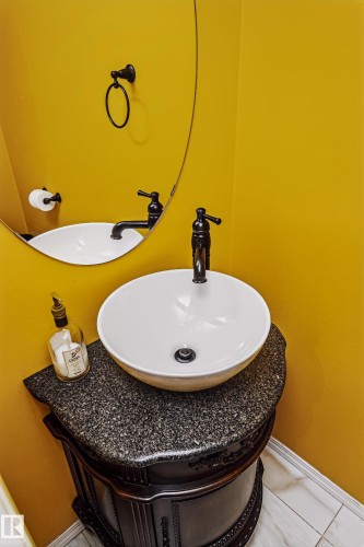 Vanity with a vessel sink, dark granite countertop, and ornate wood-finish cabinetry - #66 8304 11 Av Sw, Edmonton, AB - Indoor Photo Showing Bathroom