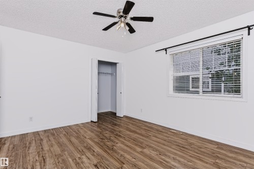 Spacious room featuring wood-finish flooring, a ceiling fan with light fixture, and a large window with blinds - #66 8304 11 Av Sw, Edmonton, AB - Indoor Photo Showing Other Room