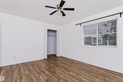 Spacious room featuring wood-finish flooring, a ceiling fan with light fixture, and a large window with blinds - 