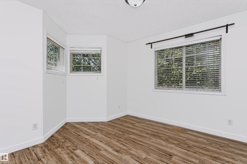 Bright interior space featuring wood-finish flooring, white walls, and multiple windows with blinds - #66 8304 11 Av Sw, Edmonton, AB - Indoor Photo Showing Other Room