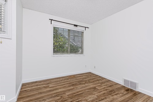 Bright interior space featuring wood-finish flooring, white walls, and a window with horizontal blinds - #66 8304 11 Av Sw, Edmonton, AB - Indoor Photo Showing Other Room