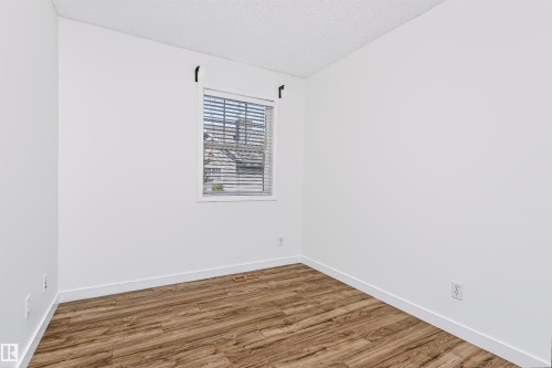 Bright room with wood-finish flooring, white baseboards, and a window with horizontal blinds - #66 8304 11 Av Sw, Edmonton, AB - Indoor Photo Showing Other Room