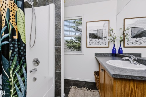 Bathroom with a white shower enclosure, chrome fixtures, and dark tiled walls - #66 8304 11 Av Sw, Edmonton, AB - Indoor Photo Showing Bathroom