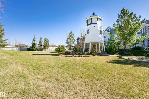 Expansive green space featuring a distinctive lighthouse-inspired structure with white siding and a blue roof accent - #66 8304 11 Av Sw, Edmonton, AB - Outdoor
