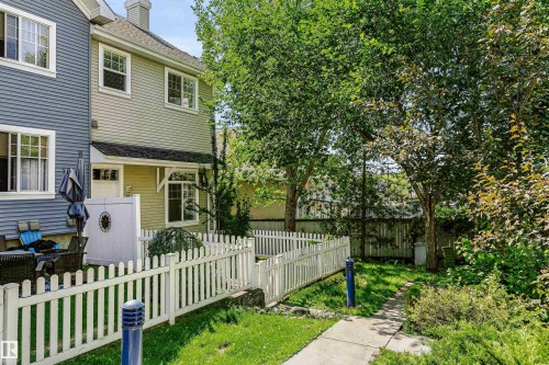 Rear exterior featuring a private patio, white picket fence, and a concrete pathway leading to a treed yard - #66 8304 11 Av Sw, Edmonton, AB - Outdoor