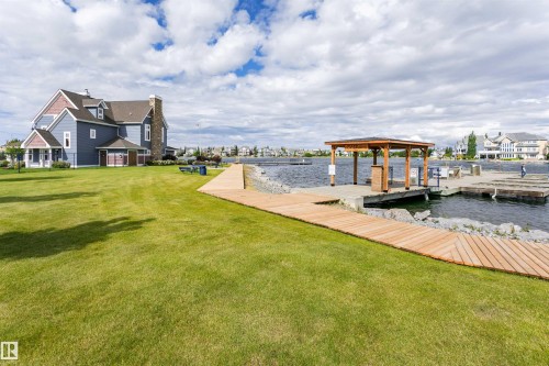 Expansive green lawn with a wooden boardwalk leading to a waterfront pier - #66 8304 11 Av Sw, Edmonton, AB - Outdoor