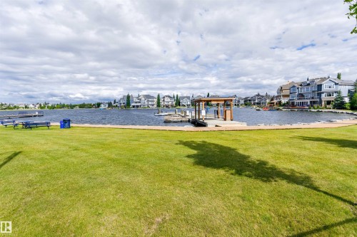 Expansive waterfront property featuring a manicured lawn, a private dock with a covered boat slip, and a stone-lined shoreline - #66 8304 11 Av Sw, Edmonton, AB - Outdoor With View