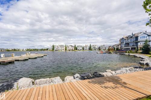 Expansive lake frontage featuring a wood plank deck, a stone retaining wall, and a multi-slip dock - #66 8304 11 Av Sw, Edmonton, AB - Outdoor With Body Of Water With View