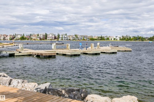 Waterfront property featuring a wooden dock system, a stone-lined shore, and a wood-finish boardwalk - #66 8304 11 Av Sw, Edmonton, AB - Outdoor With Body Of Water With View
