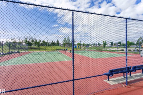 Tennis court featuring a hard surface, red and green playing area, chain-link fencing, and integrated benches - #66 8304 11 Av Sw, Edmonton, AB - Outdoor With Deck Patio Veranda