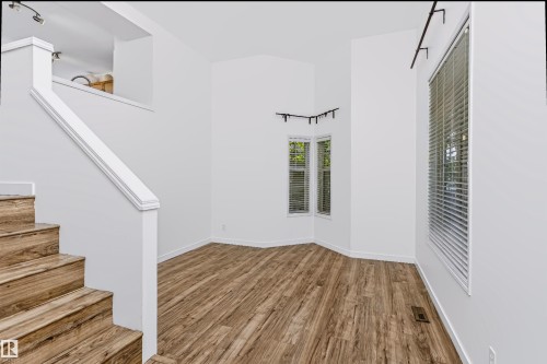 Open-concept room featuring wood-finish flooring, white walls, and a prominent staircase with matching wood-finish treads and white risers - #66 8304 11 Av Sw, Edmonton, AB - Indoor Photo Showing Other Room