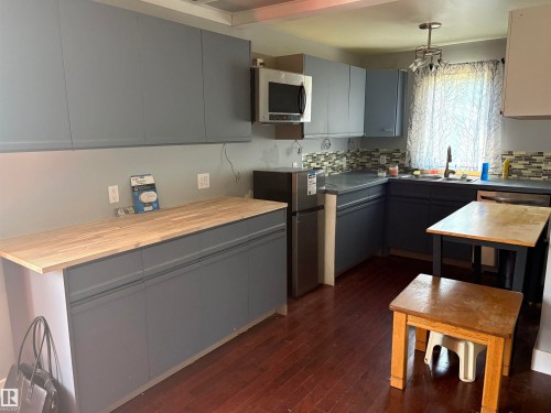 Modern kitchen featuring dark wood-finish flooring, gray cabinetry, butcher block countertops, a stainless steel microwave, and a tiled backsplash - 4620 Maria Drive, Smoky Lake Town, AB - Indoor Photo Showing Kitchen