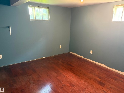 Spacious room featuring rich wood-finish flooring, contemporary blue-gray wall paint, and two distinct windows - 4620 Maria Drive, Smoky Lake Town, AB - Indoor Photo Showing Other Room