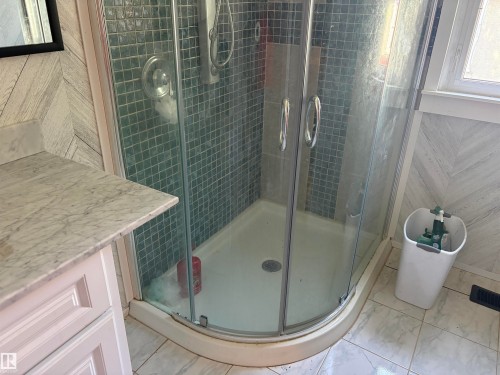 Corner glass-enclosed shower with teal mosaic tile surround, featuring a chrome shower fixture - 4620 Maria Drive, Smoky Lake Town, AB - Indoor Photo Showing Bathroom