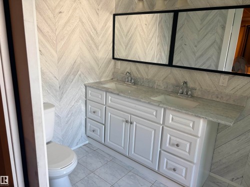 Bathroom featuring a dual vanity with white cabinetry and chrome hardware, a light-toned countertop, and two framed mirrors - 4620 Maria Drive, Smoky Lake Town, AB - Indoor Photo Showing Bathroom