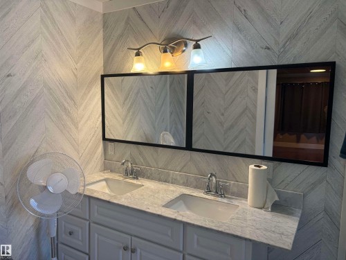 Dual sink vanity with light gray cabinetry, a stone-finish countertop, and chrome fixtures - 4620 Maria Drive, Smoky Lake Town, AB - Indoor Photo Showing Bathroom