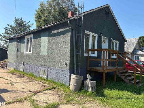stucco exterior featuring white-framed windows, a wood deck with stairs, a white entry door, and two exterior wall-mounted light fixtures - 4620 Maria Drive, Smoky Lake Town, AB - Outdoor