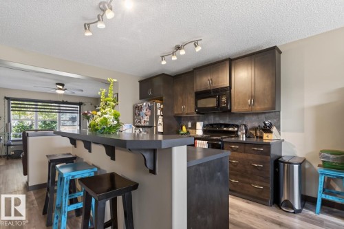 Kitchen featuring dark cabinetry, black appliances including a built-in microwave, and a breakfast bar with an extended countertop - 3627 12 Street Nw, Edmonton, AB - Indoor Photo Showing Kitchen