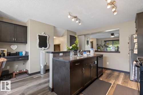 Kitchen island with a double basin sink, dark wood-finish cabinetry, and track lighting - 3627 12 Street Nw, Edmonton, AB - Indoor Photo Showing Kitchen With Double Sink