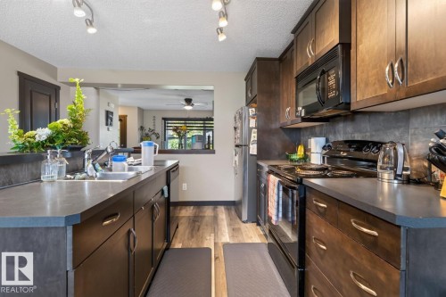 Full kitchen featuring wood-finish cabinetry, dark countertops, and a stainless steel double-basin sink - 3627 12 Street Nw, Edmonton, AB - Indoor Photo Showing Kitchen With Double Sink