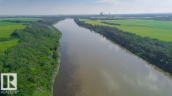 River frontage with a natural treeline on both banks, bordered by expansive green fields - 