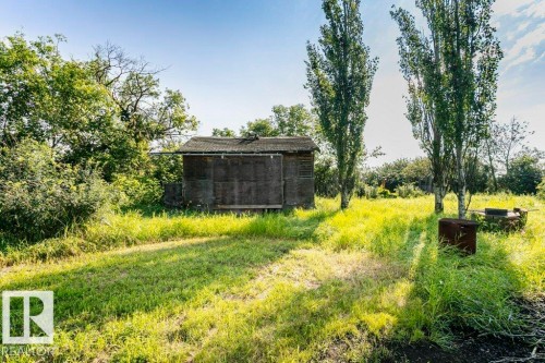 Rural property featuring a standalone shed with a dark exterior and a sloped roof, surrounded by mature trees and overgrown grass - 55319 Rge Road 222, Rural Sturgeon County, AB 