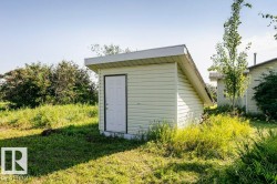 Detached utility shed featuring light-colored siding, a white panel door, and a sloped roof - 