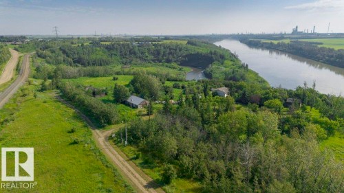 Aerial property overview featuring two residential structures nestled within lush green foliage, extensive land, and direct river frontage - 55319 Rge Road 222, Rural Sturgeon County, AB 