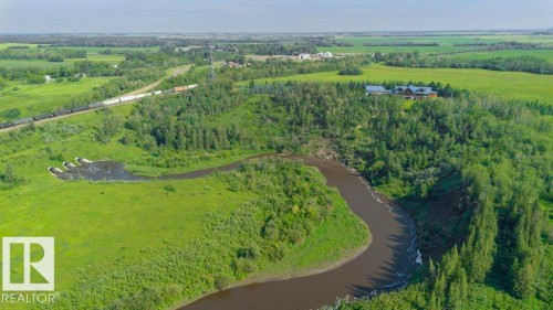 Expansive green landscape featuring a curving waterway, dense tree lines, and distant structures - 55319 Rge Road 222, Rural Sturgeon County, AB 