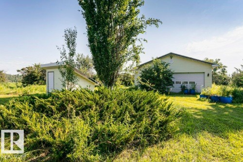 Expansive green space featuring a detached garage with a white roll-up door, a separate outbuilding with a white entry door, and mature trees - 55319 Rge Road 222, Rural Sturgeon County, AB 