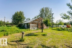 Wood-sided outbuilding with a metal roof, set within a grassy expanse featuring mature trees and additional structural elements - 