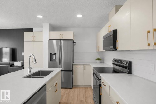 Modern kitchen featuring white cabinetry with gold-tone hardware, stainless steel appliances, light-toned countertops, and wood-finish flooring - #42 19904 31 Av Nw, Edmonton, AB - Indoor Photo Showing Kitchen With Double Sink With Upgraded Kitchen