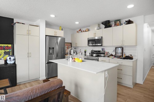 Modern kitchen featuring a central island with a solid surface countertop, stainless steel appliances, extensive cabinetry, a tiled backsplash, and recessed lighting - #42 19904 31 Av Nw, Edmonton, AB - Indoor Photo Showing Kitchen With Double Sink